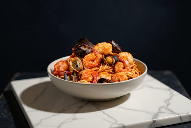 Seafood pasta with shrimp, mussels, and clams in a white bowl on a marble slab.